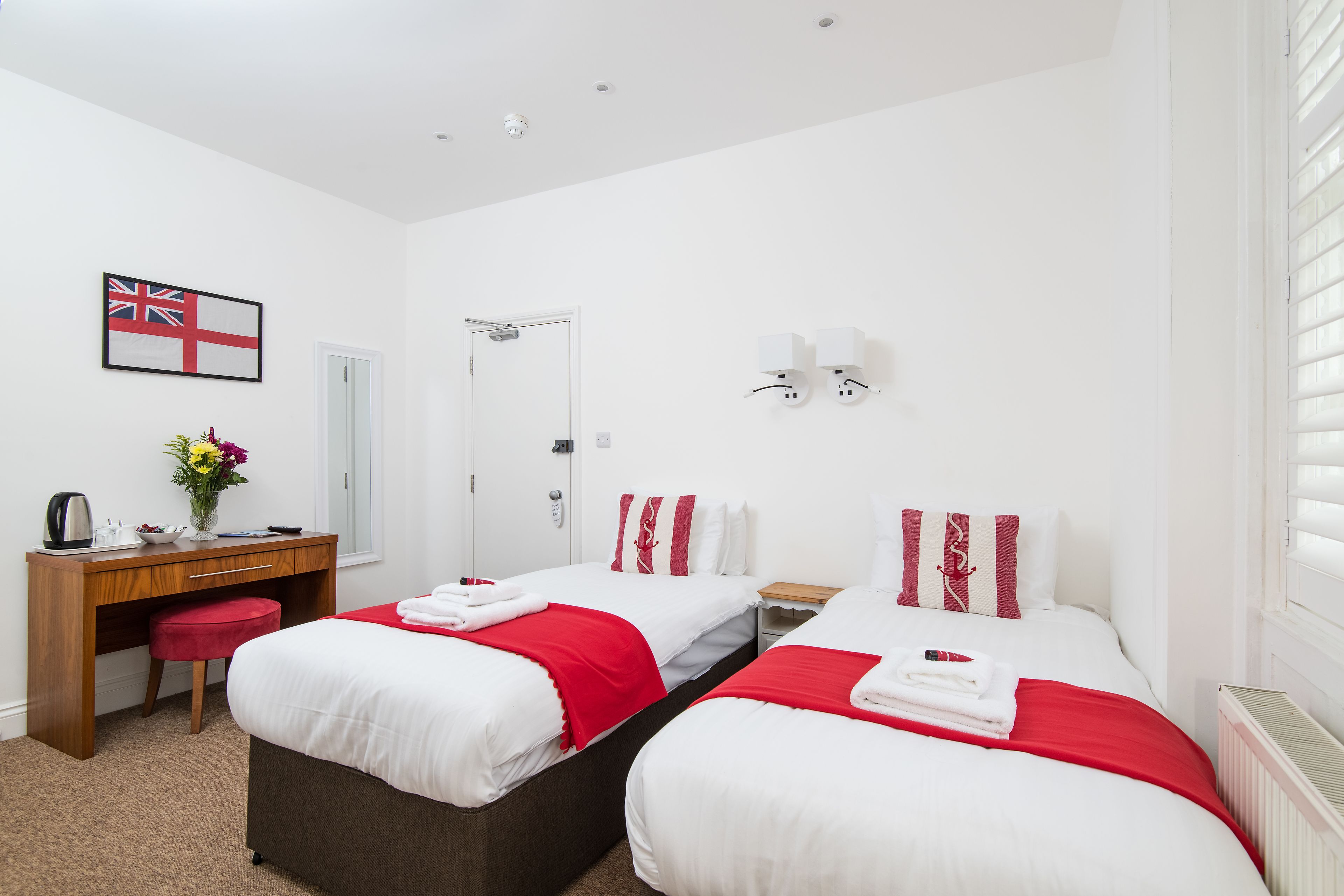 A hotel room with two beds, a desk, a chair, a radiator, and a flag on the wall.