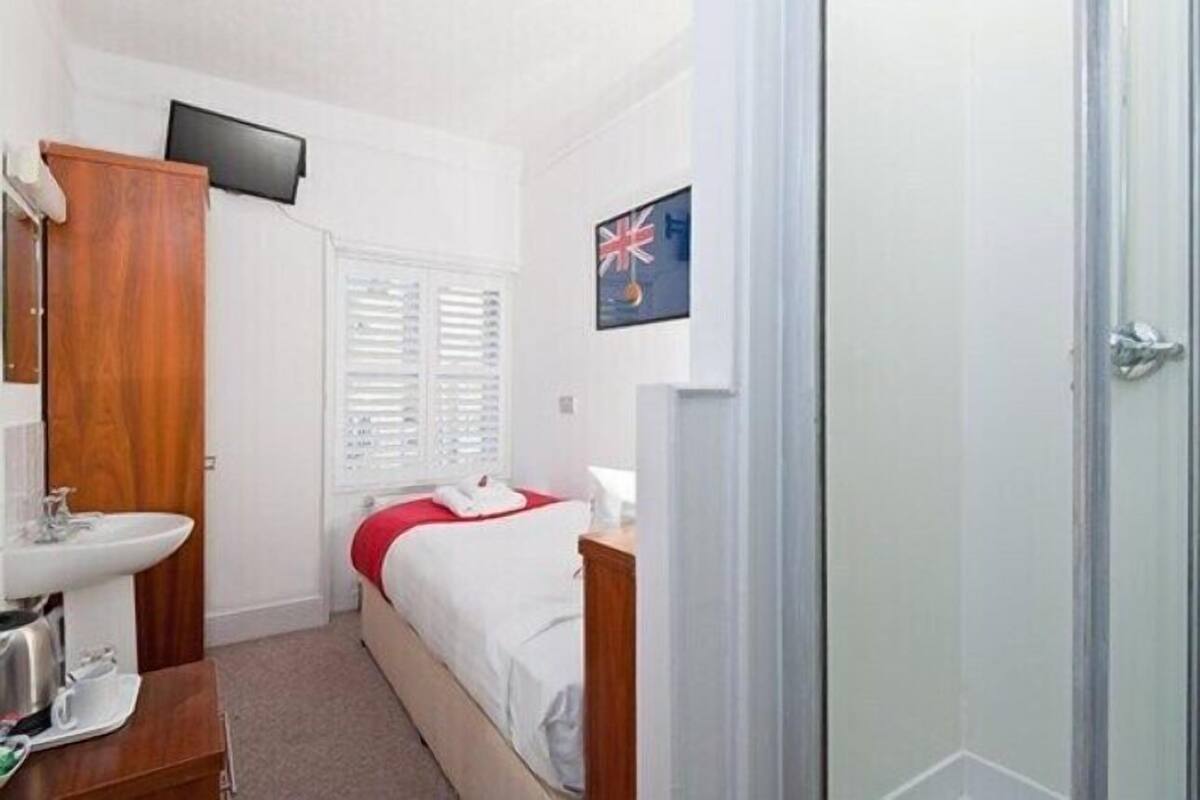 A hotel room with a bed, a bedside table, a mirror, a sink, a television mounted on the wall, and a door leading to another room.