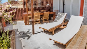 Un patio con una mesa y sillas de madera, una tumbona y una pérgola.