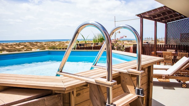 Una piscina de madera con escaleras de metal, sillas de descanso y vistas a la playa.