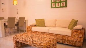 Una sala de estar con un sofá de mimbre, un reposapiés a juego, un comedor con sillas y una obra de arte colgada en la pared.