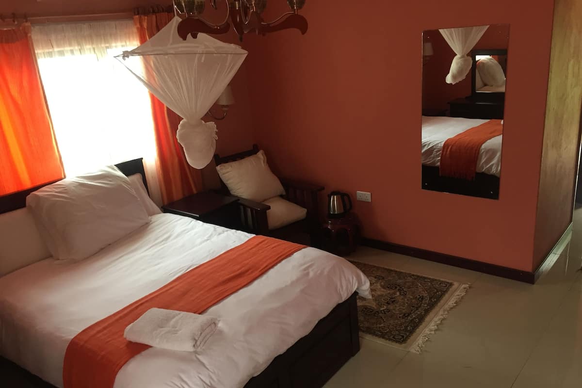 A neatly made bed with white and orange bedding, a bedside table with a lamp, and a mirror on the wall.