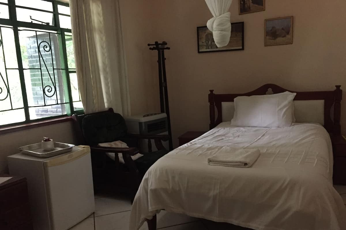 A bedroom with a bed, a chair, a small table, and a window with curtains.