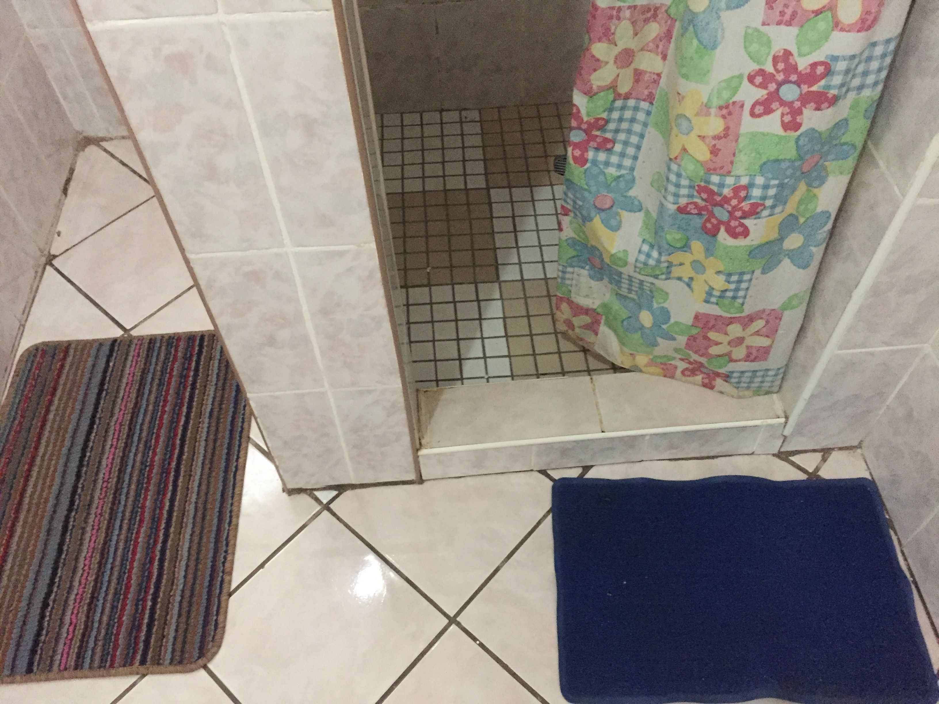 A bathroom with a tiled floor, a striped rug, a blue bath mat, and a shower curtain with a floral pattern.