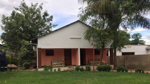A single-story house with a flat roof, a porch with a bench, and a small garden area in front. - Divine Guest House (Livingstone)