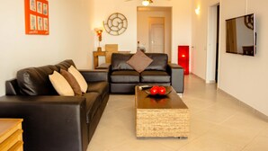 A modern living room with a black leather sofa, a woven coffee table, and a ceiling fan. - Antonio Sousa Beach 3 Bedroom Apartment (Sal)