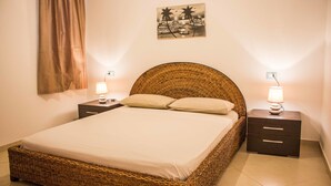A neatly made bed with a woven headboard, two bedside tables with lamps, and a wall-mounted picture. - Antonio Sousa Beach 3 Bedroom Apartment (Sal)