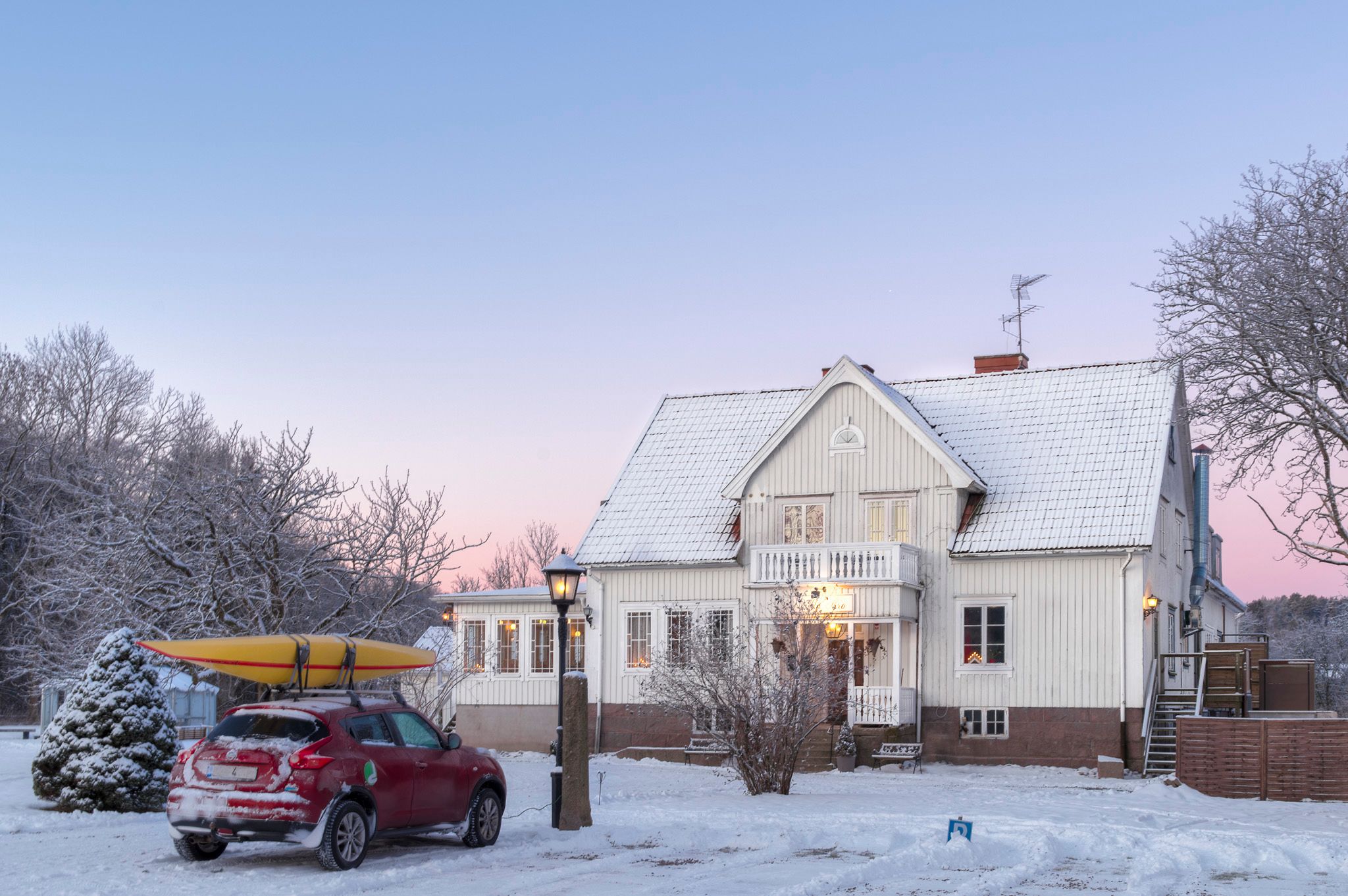 A white building with a snow-covered roof and a red car parked in front.