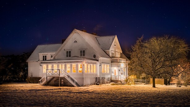A large, two-story house with a prominent staircase leading to the upper floor, a balcony, and a well-lit front porch. - Villa Bro (Brastad)