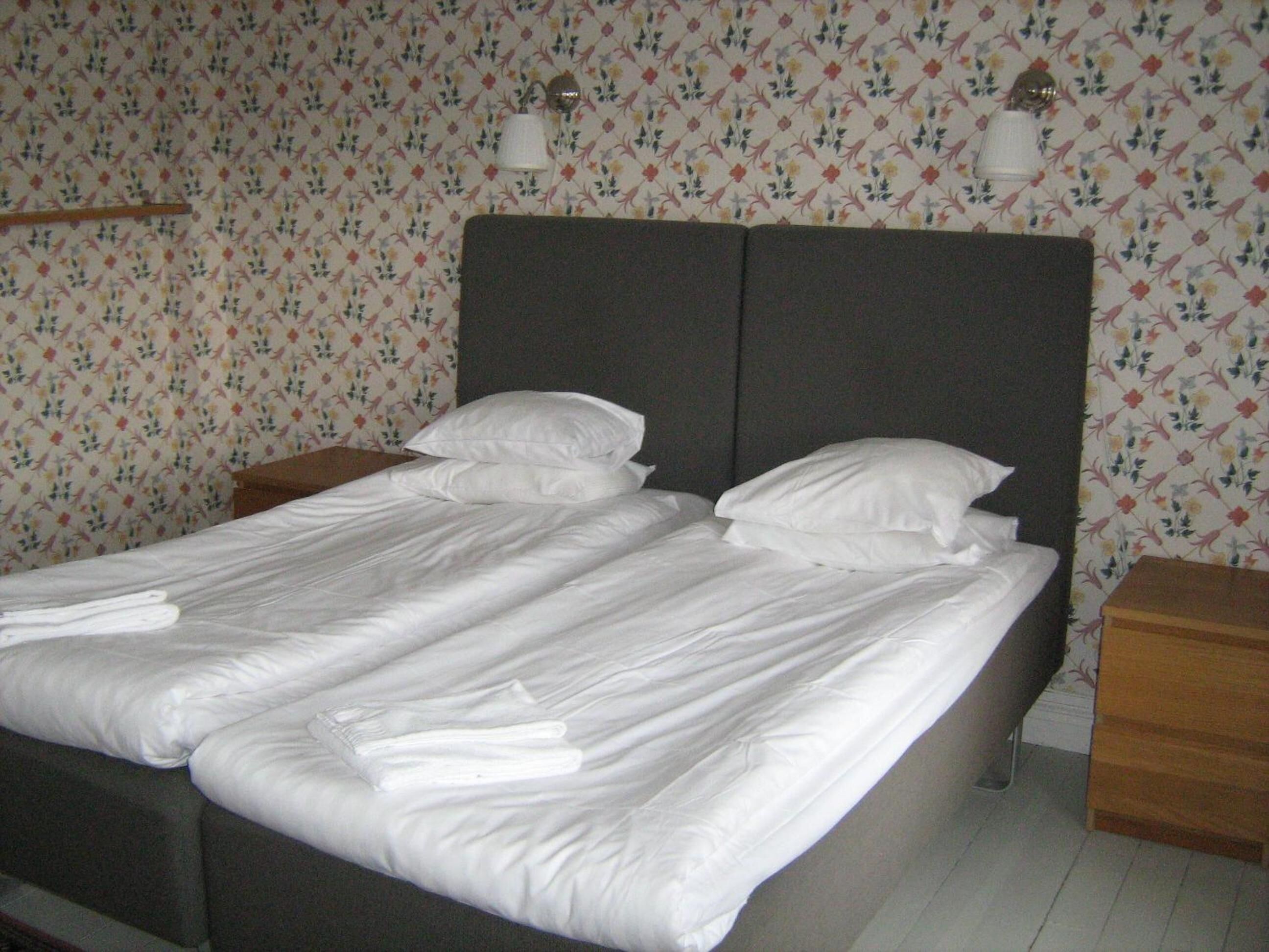 A double bed with white linens, two bedside tables, and floral wallpaper.