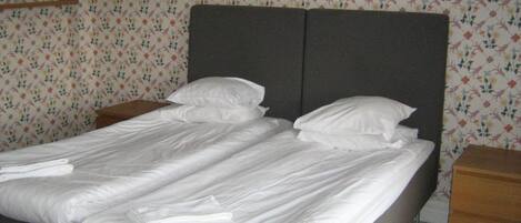 A double bed with white linens, two bedside tables, and floral wallpaper.