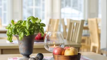 A dining table with a potted basil plant, a bowl of apples, and a candle.