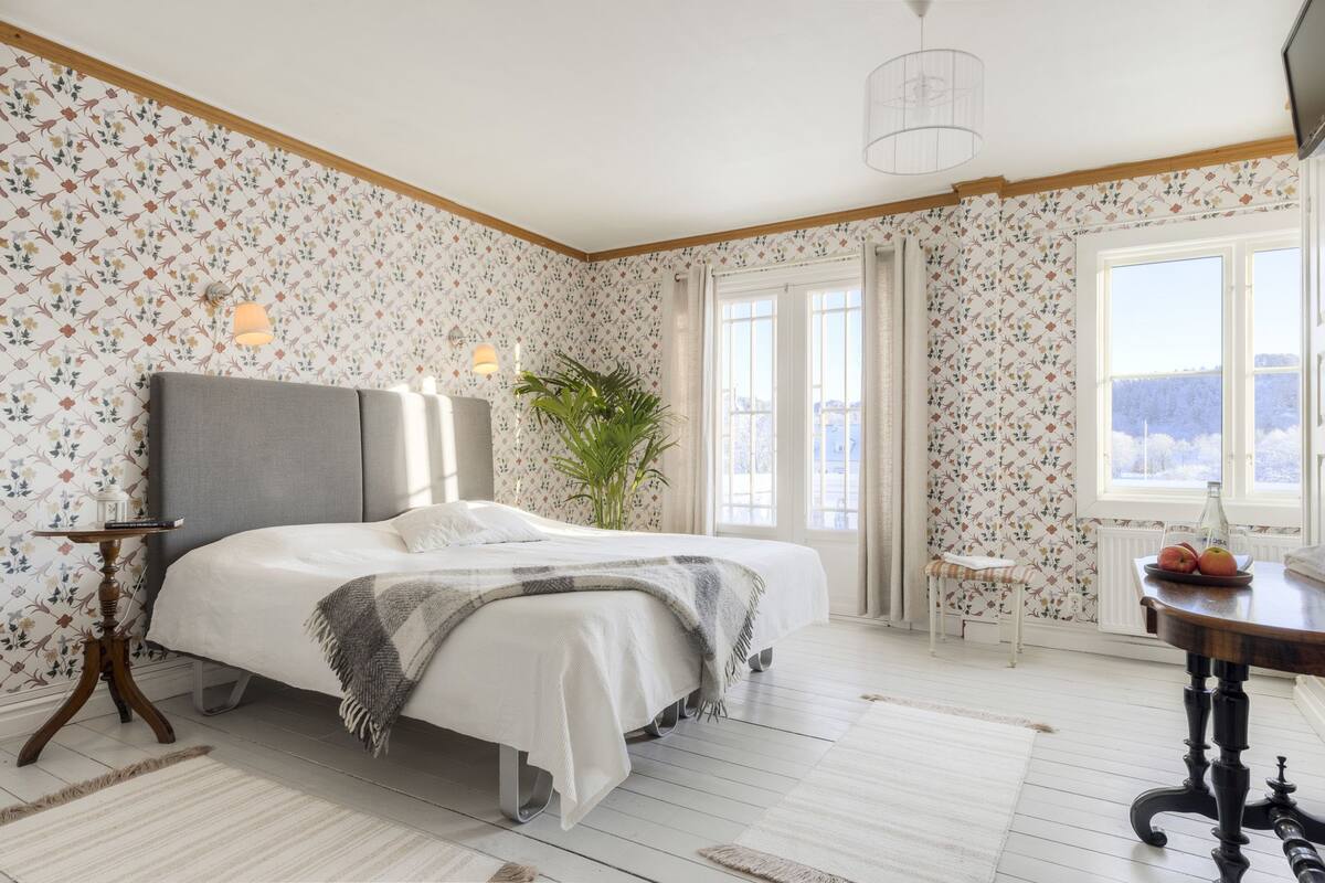 A bedroom with a bed, a bedside table, a chair, a window, and a view of the outdoors.