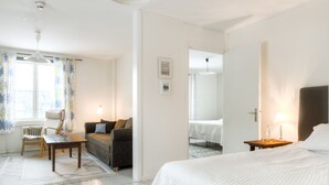 A hotel room with a bed, a sofa, a table, and a chair. There is a window with curtains, a lamp, and a picture on the wall. - Villa Bro (Brastad)