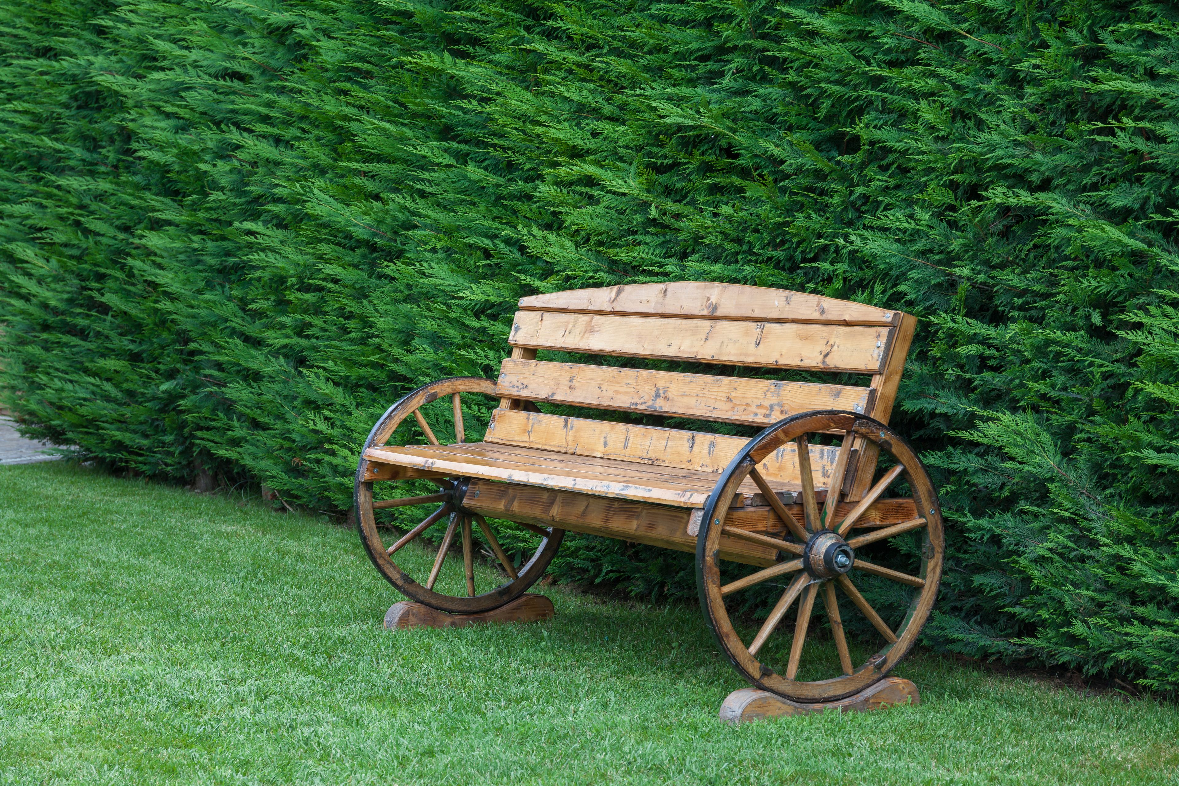 Eine Parkbank mit großen Rädern, auf einer Rasenfläche vor einer dichten, grünen Hecke.
