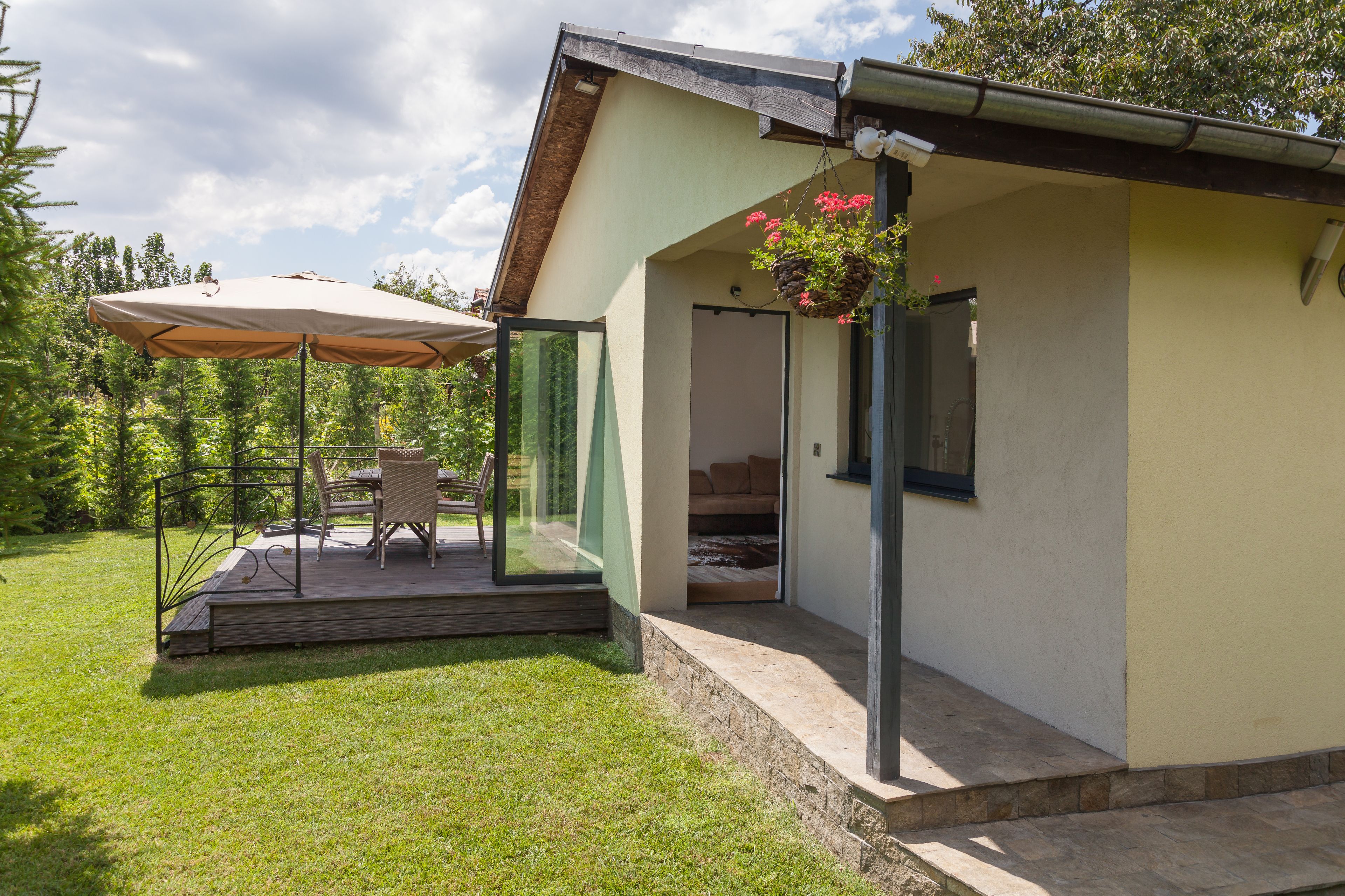 Ett modernt hus med en täckt uteplats, en matplats med utemöbler och en hängande blomkorg.
