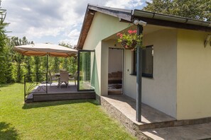 A modern house with a covered patio, a dining area with outdoor furniture, and a hanging flower basket. - Cherry Tree Cottage (Varna)