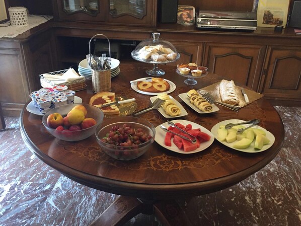 A breakfast buffet with various fruits, pastries, and desserts on a wooden table.