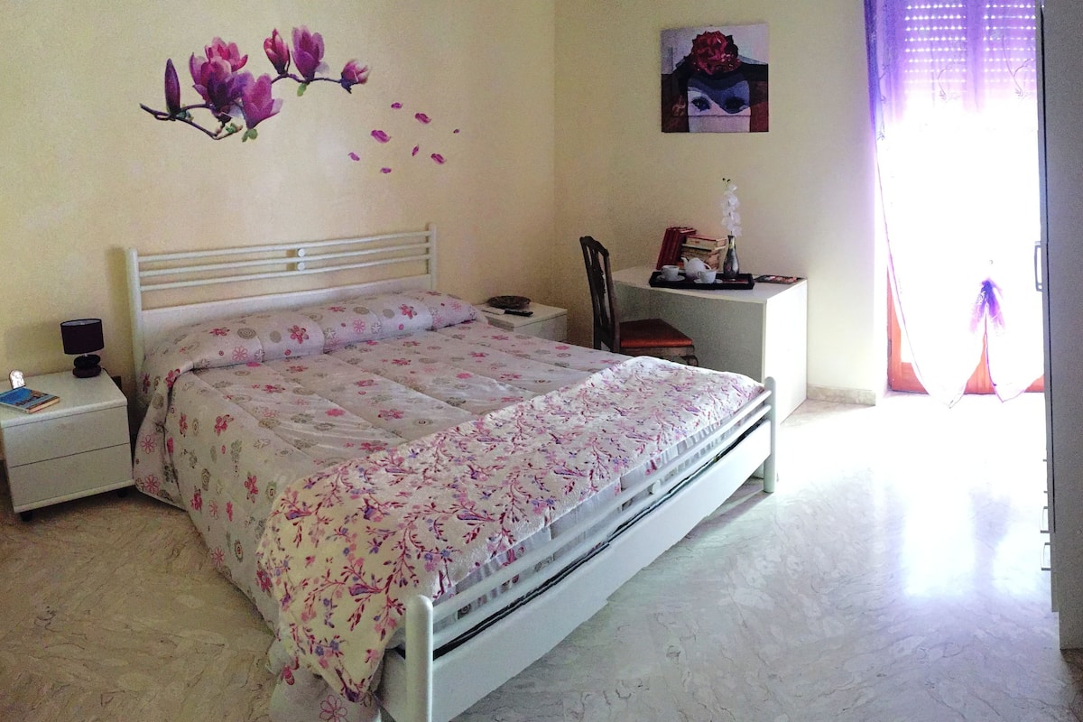 A bedroom with a bed, nightstand, chair, and a desk with a lamp.