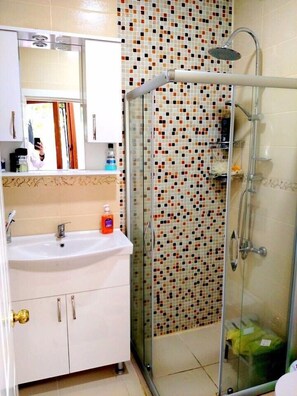 Um banheiro com chuveiro em cabine de vidro, pia branca e painel de azulejos.
