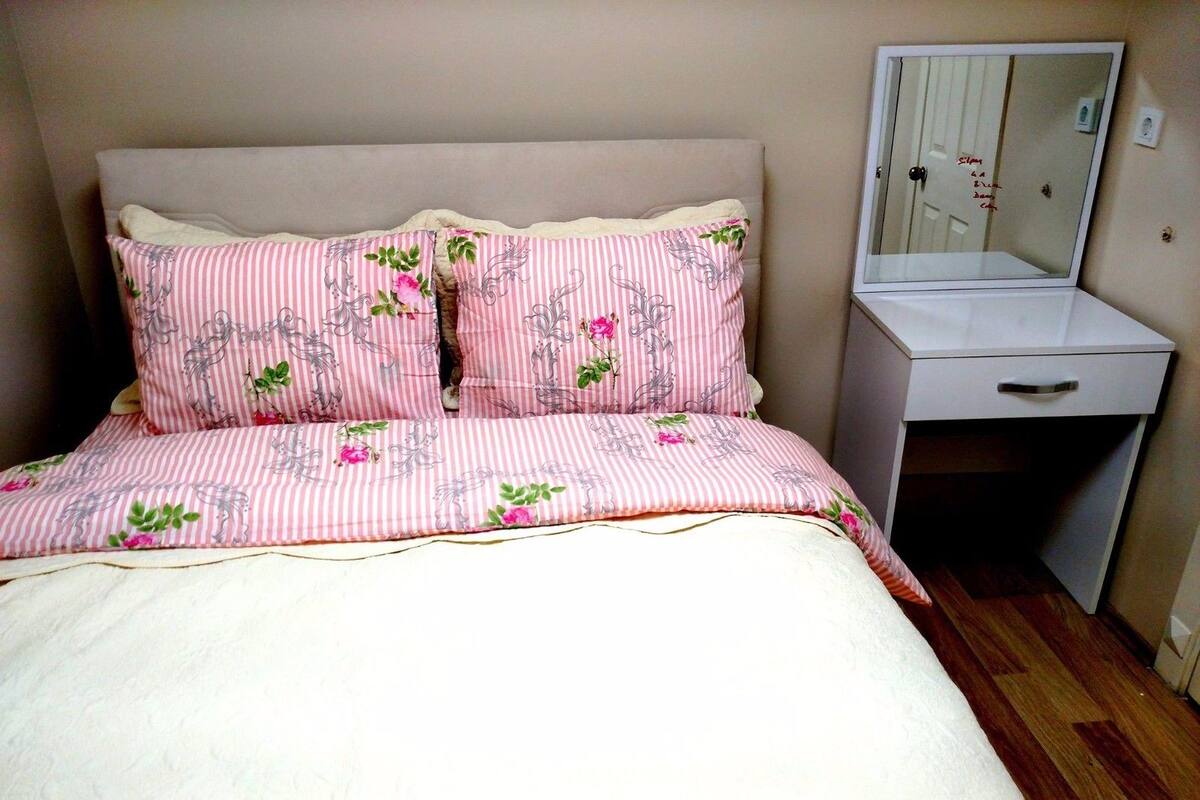 A bedroom with a bed, two pillows, a bedside table, and a mirror.