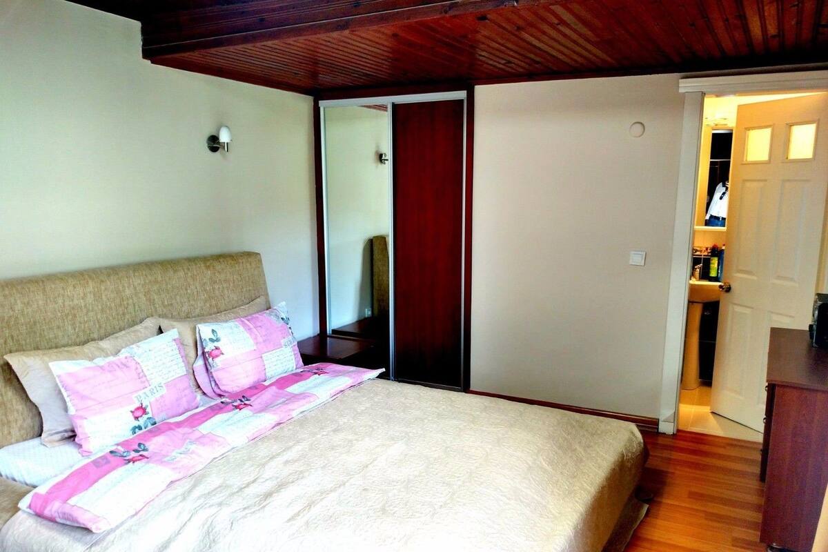 A bedroom with a bed, a wooden ceiling, a wardrobe, and a door leading to a bathroom.