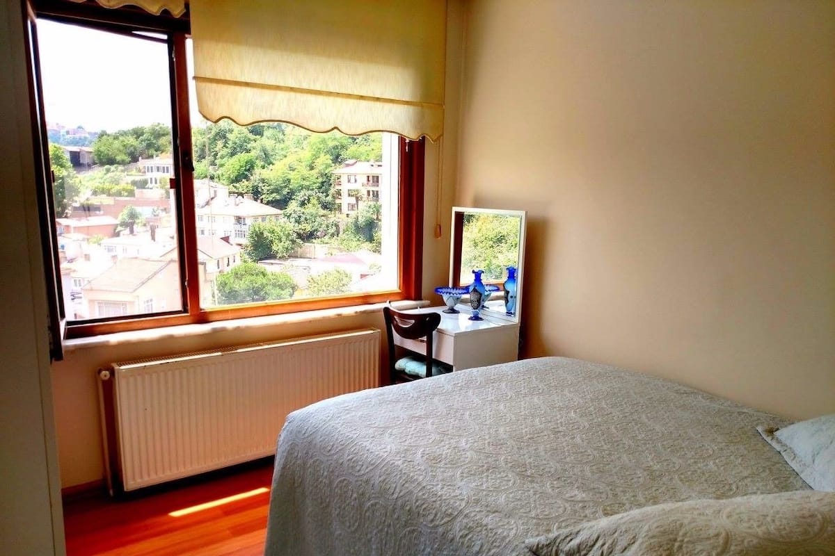 A bedroom with a large window, a bed, a desk, and a chair.