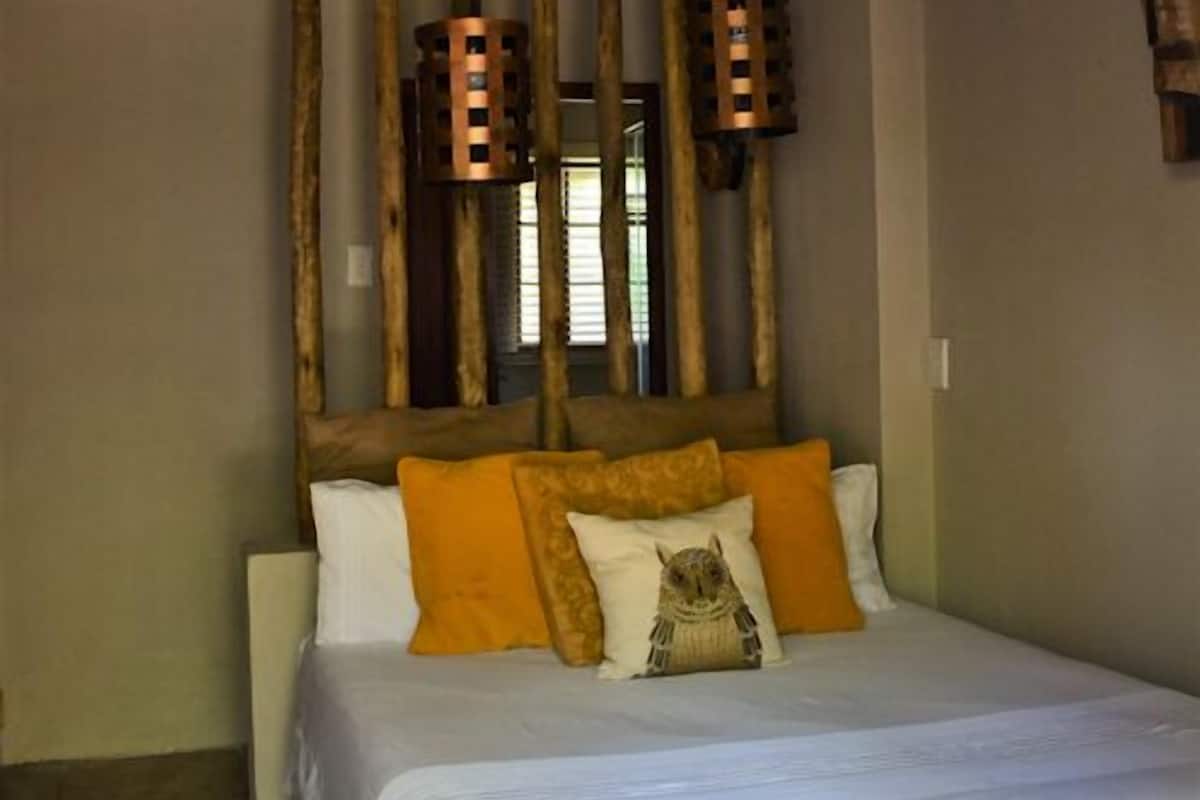 Ein Bett mit weißer Bettwäsche, einem Holz-Kopfteil und orangefarbenen Kissen.