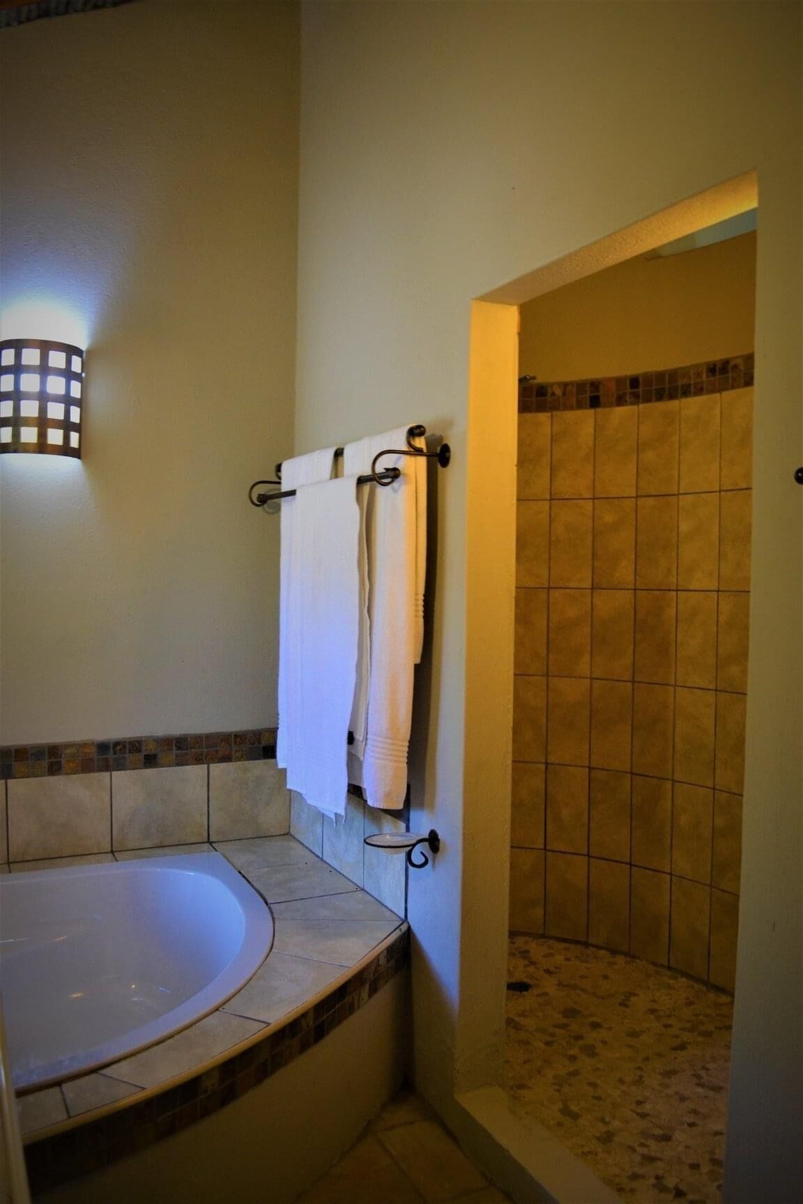 A bathroom with a bathtub, a towel rack with towels, a wall-mounted light fixture, and a shower area with tiled walls.