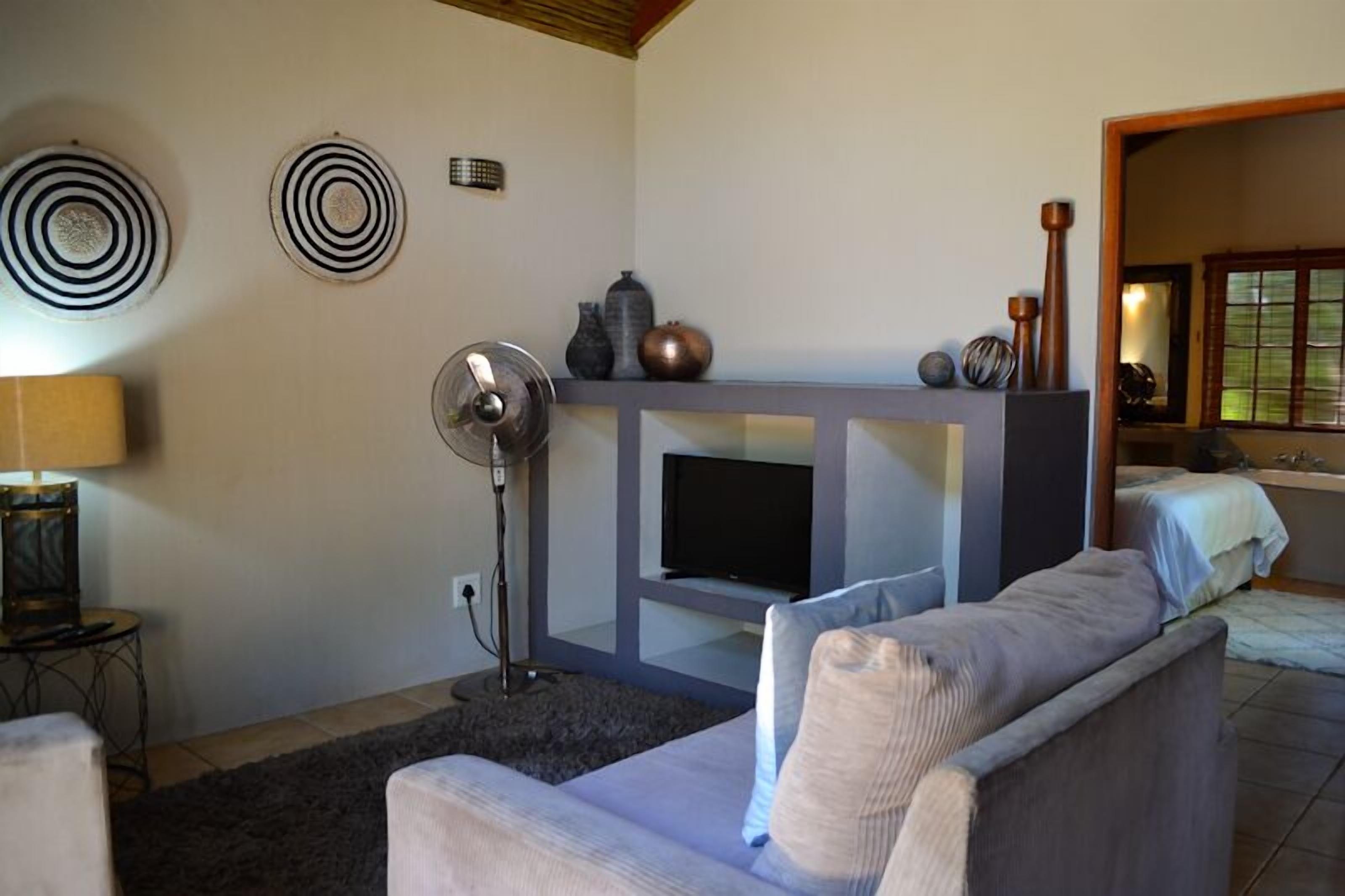 Un salon comprenant un canapé, un téléviseur, un ventilateur, des vases décoratifs et une cheminée.