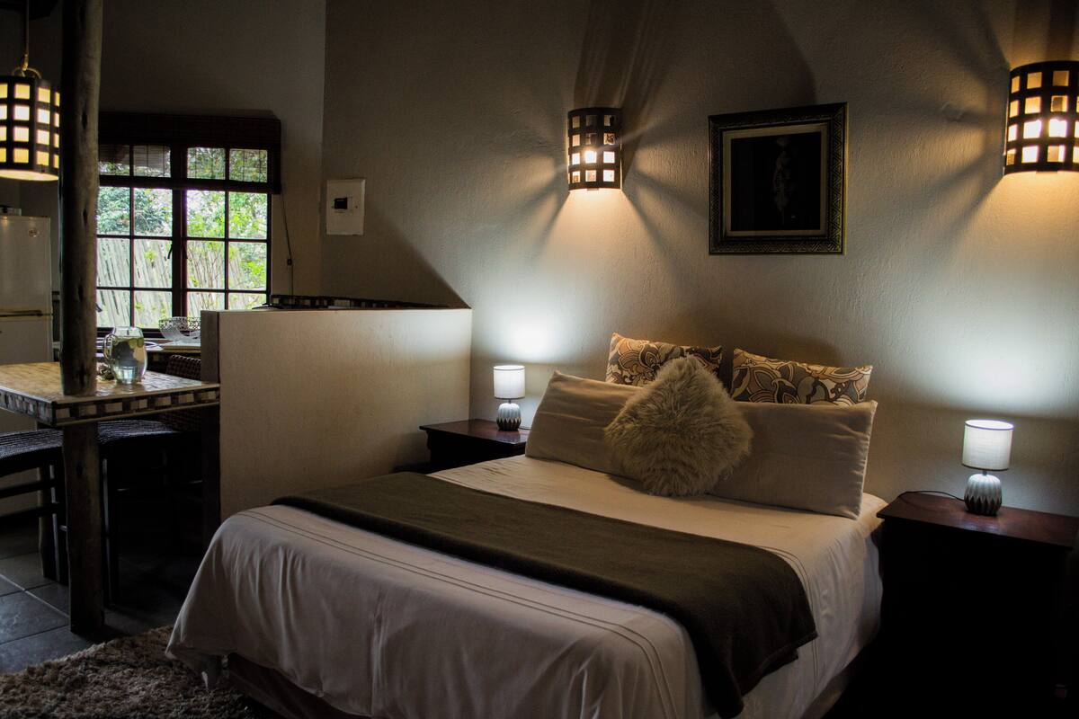 Ein Schlafzimmer mit Bett, Nachttischlampen, einem Nachttisch, einem Fenster und einem Schreibtisch mit Stuhl.