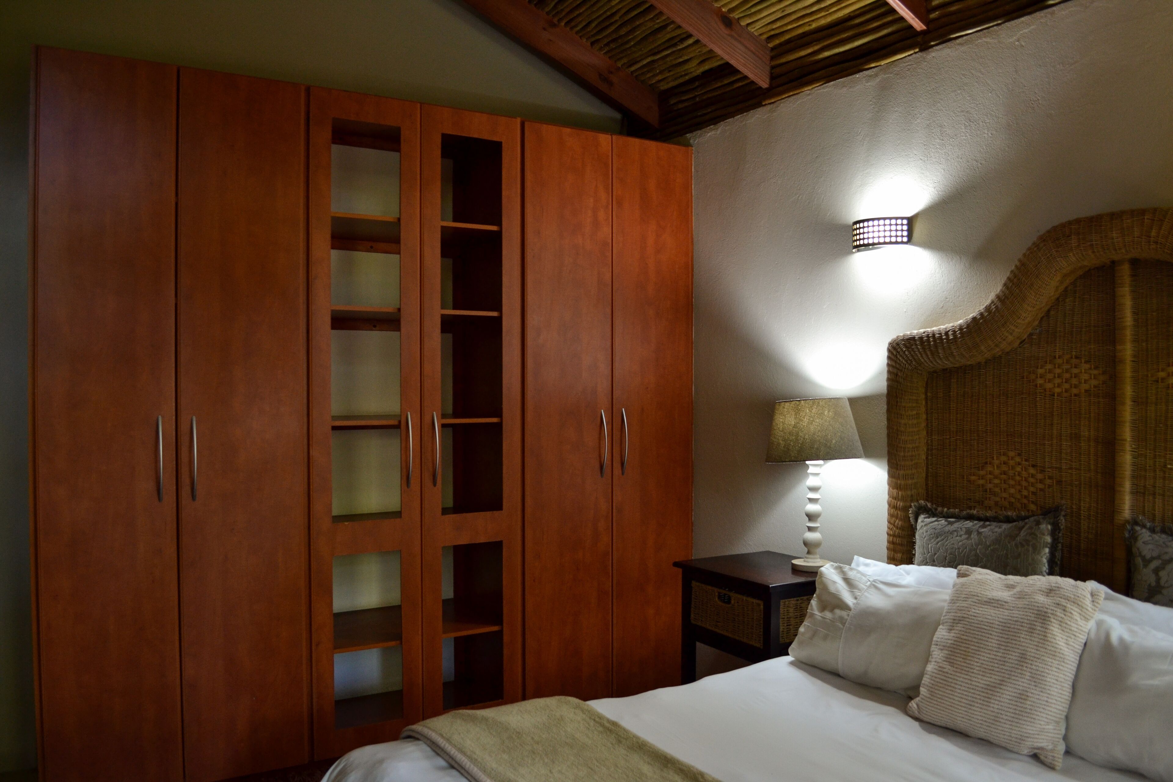 Un dormitorio con un armario de madera, una cama con almohadas, una mesita de noche y una lámpara de pared.