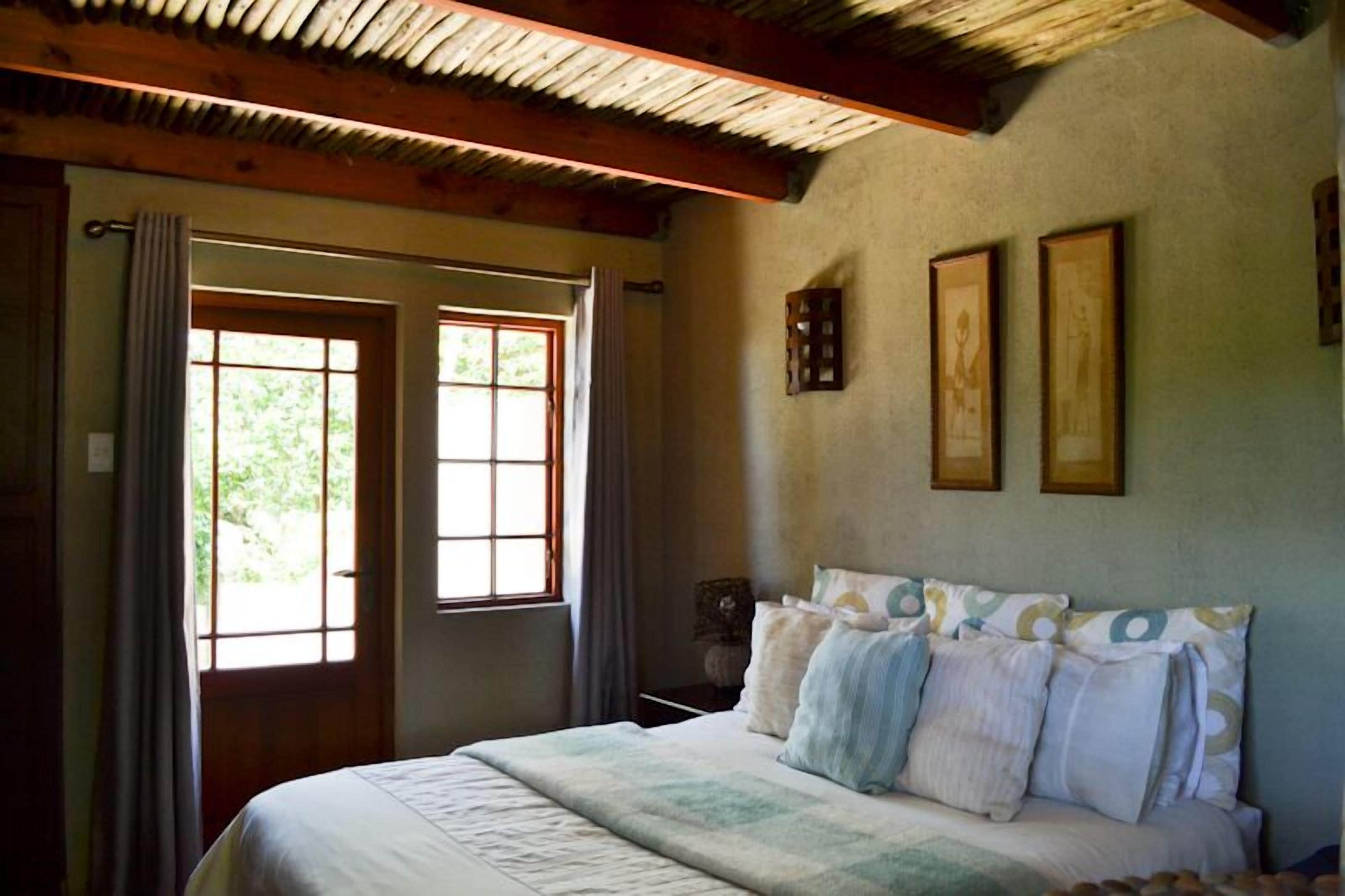 A bedroom with a bed, two windows, a wooden ceiling, and framed pictures on the wall.