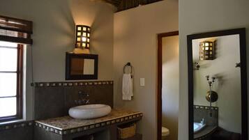 Un baño con lavamanos blanco, un espejo, un perchero para toallas e iluminación en la pared.