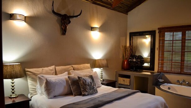 Een slaapkamer met een bed, nachtlampjes, een spiegel aan de muur, een grote spiegel, een raam met jaloezieën en een schedel van een stier aan de muur.