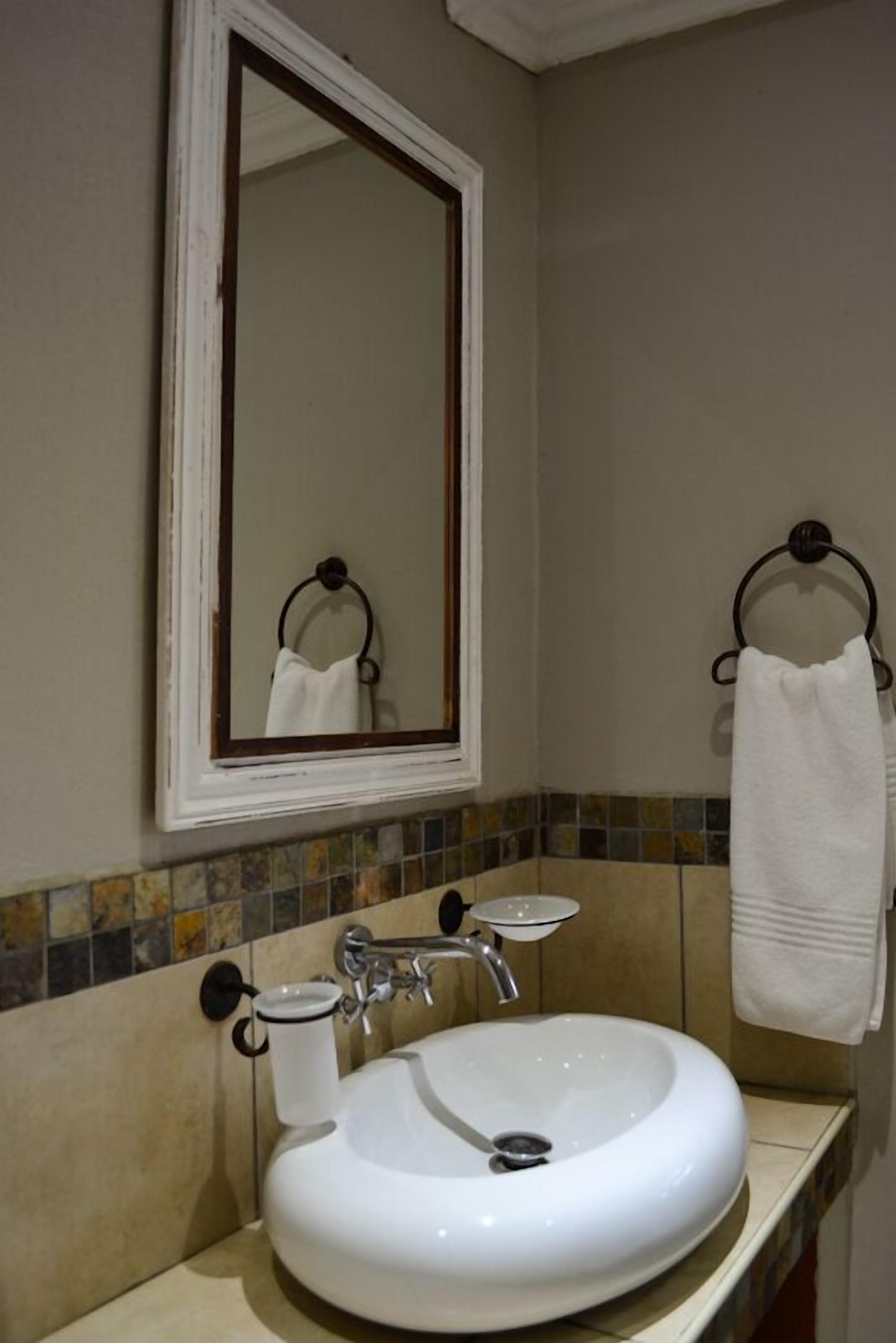 Une salle de bain avec un lavabo blanc, un miroir et deux porte-serviettes.