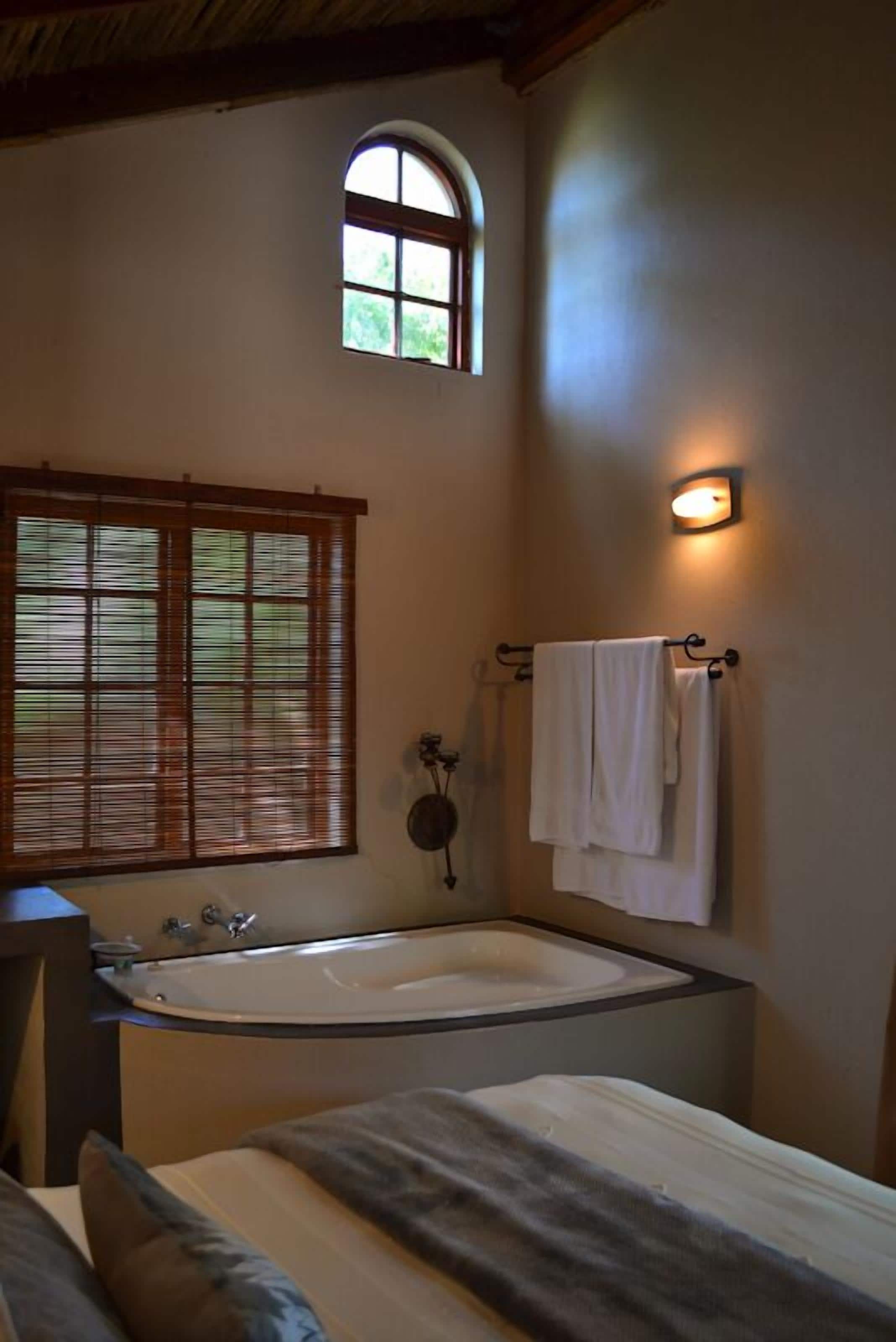 A bathroom with a freestanding bathtub, a window with blinds, a towel rack, and a wall-mounted light fixture.