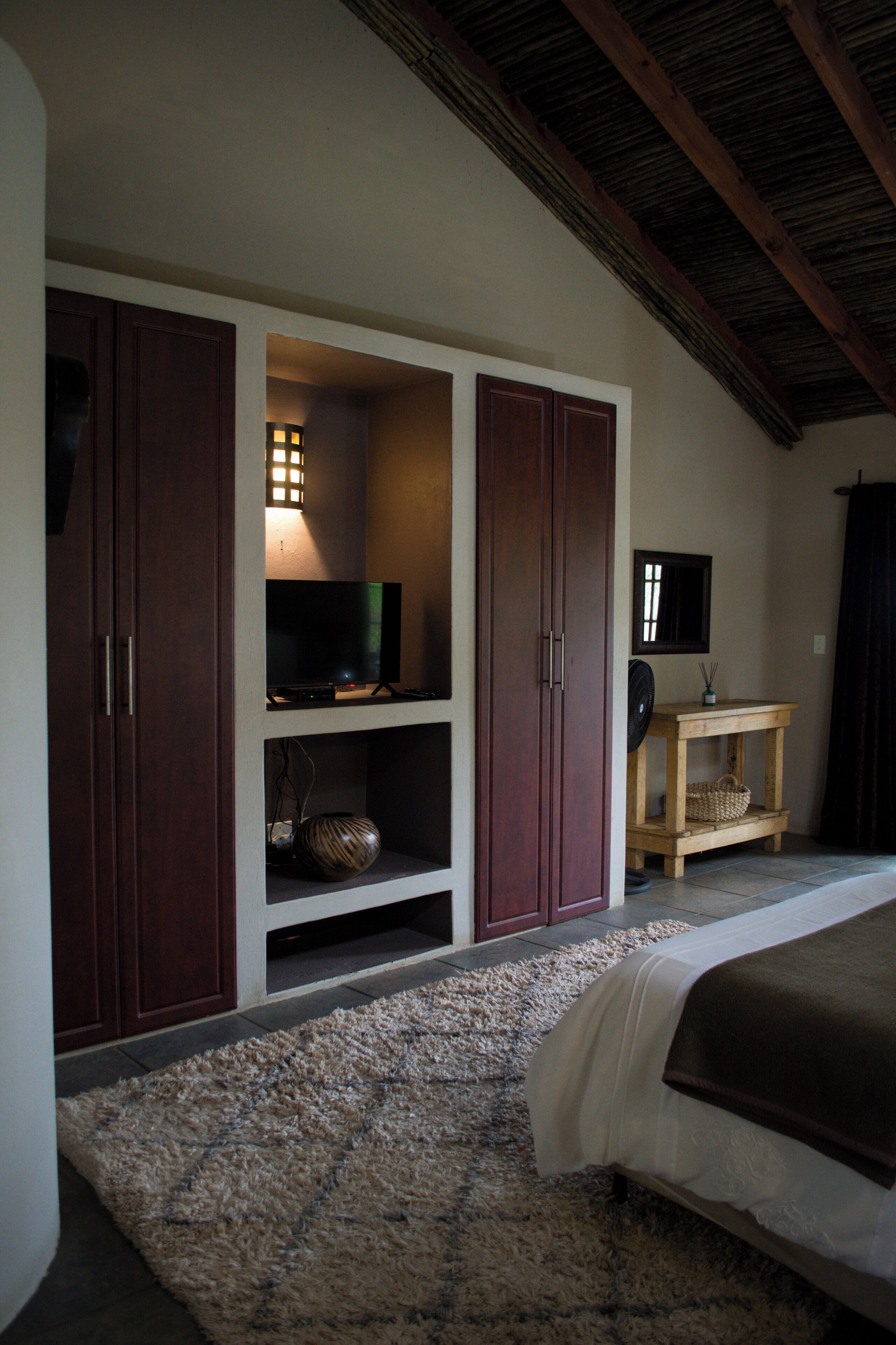 A bedroom with a bed, a television on a shelf, and a wooden table with a basket.