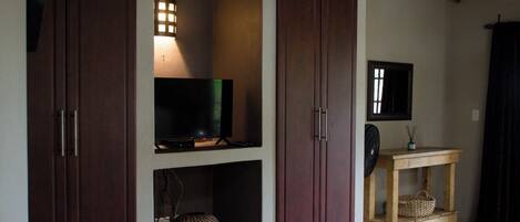 A bedroom with a bed, a television on a shelf, and a wooden table with a basket.