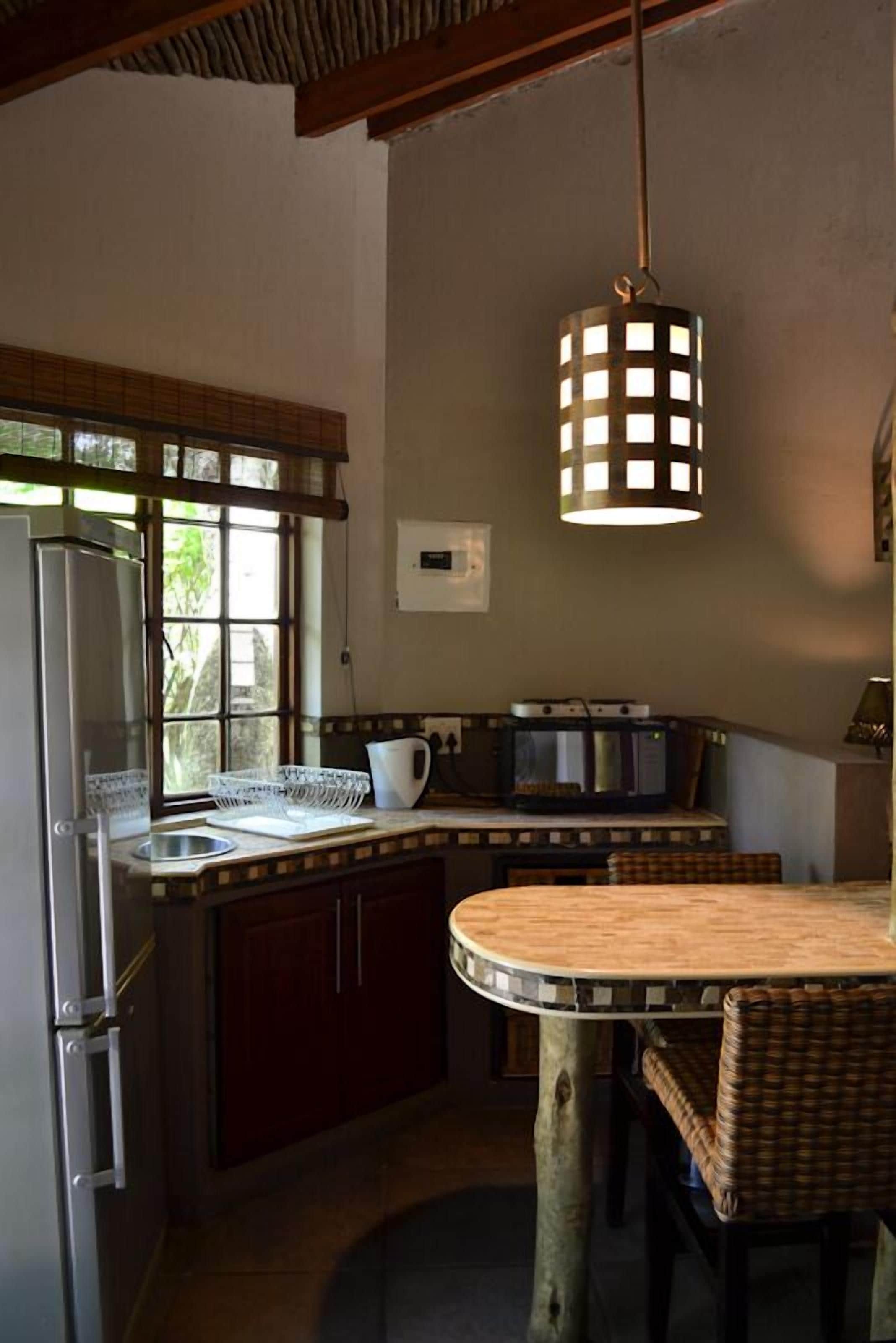 Una cocina compacta con refrigerador, microondas y un pequeño comedor con sillas de mimbre.