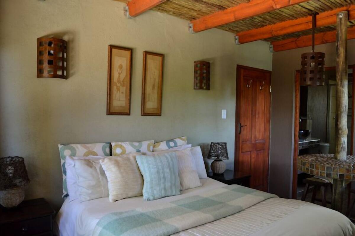Ein Schlafzimmer mit einem Bett, zwei gerahmten Bildern, einer Holztür und einem Essbereich mit Tisch und Stühlen.