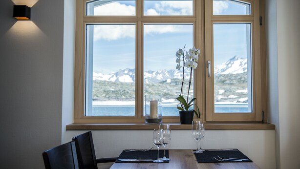 Un comedor con una mesa preparada para dos, una planta en maceta y una vela en el alféizar de la ventana.