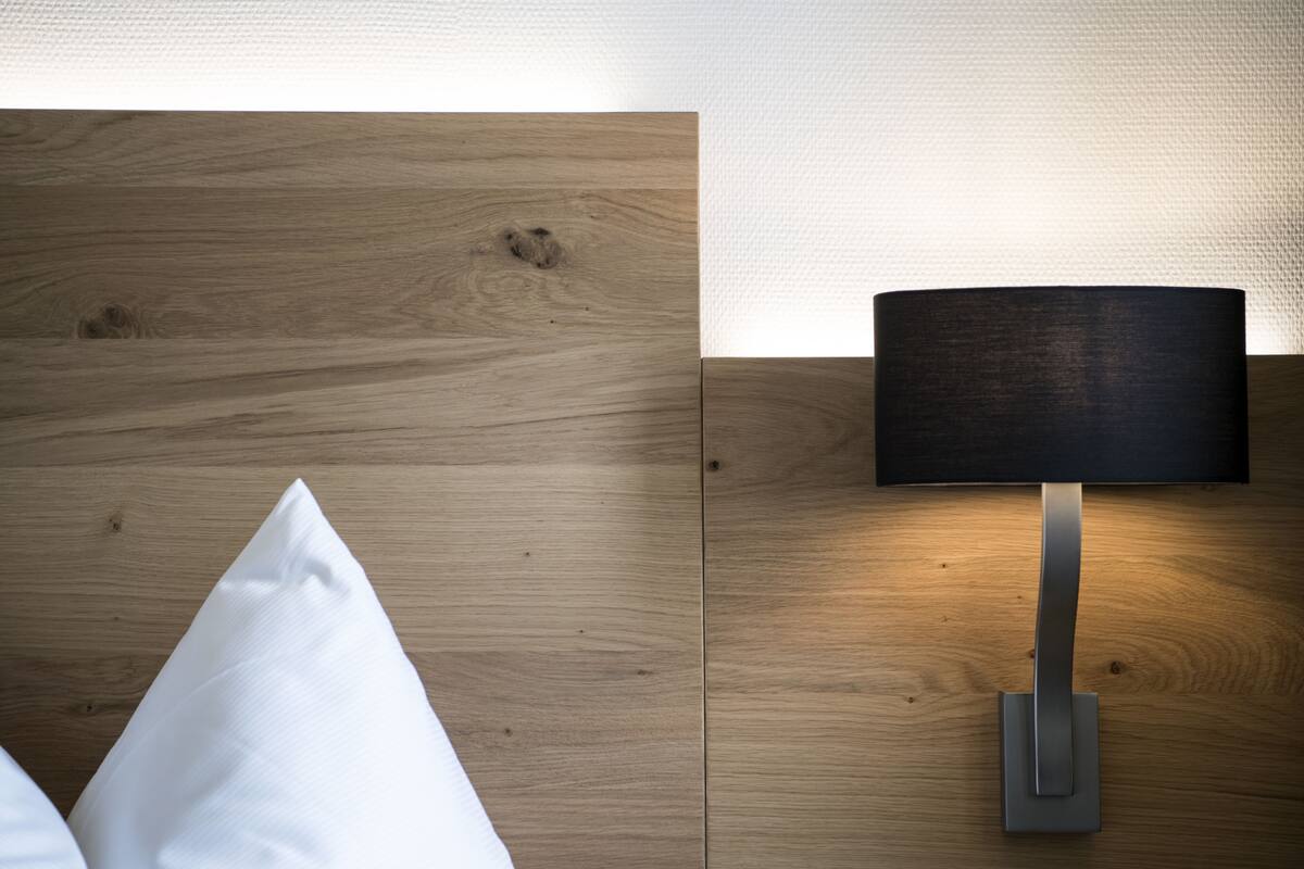Un dormitorio moderno con cabecera de madera, lámpara de noche y almohada blanca.