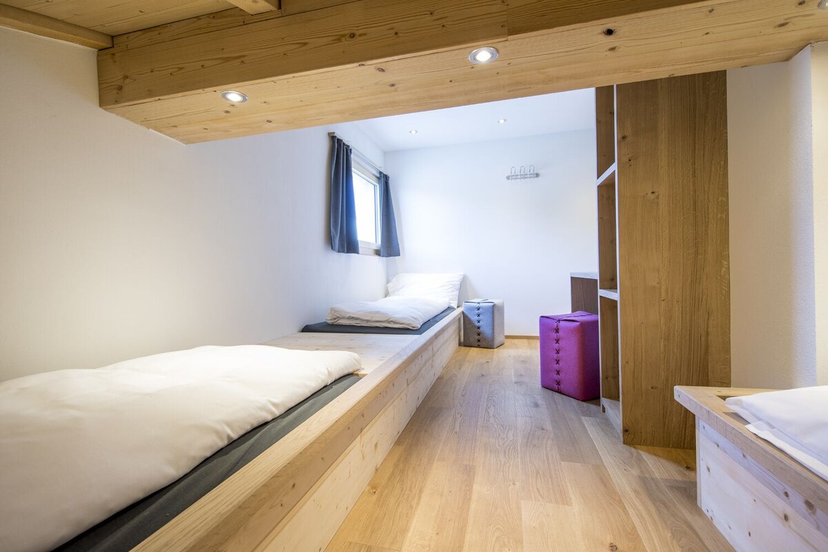 Una habitación pequeña y acogedora con dos camas de madera, una ventana con cortinas y techo de madera.