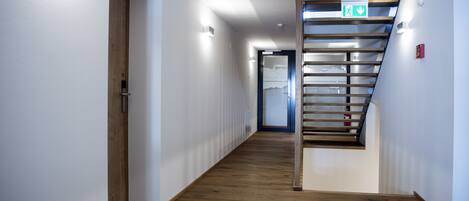 Un couloir moderne avec un plancher en bois, un escalier doté d’une rampe en verre et une porte portant le numéro 12.