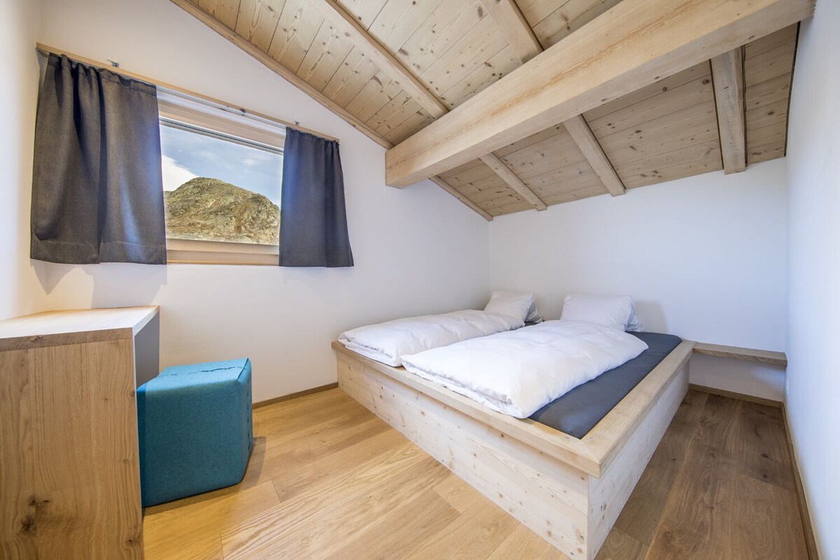 Un dormitorio con una cama litera de madera, un escritorio pequeño y una ventana con cortinas.