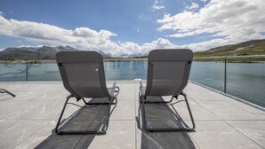 Dos sillones de descanso frente a una extensa masa de agua con montañas al fondo.