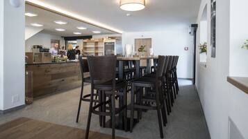 Un espace repas moderne avec une longue table en bois et des chaises foncées, un coin bar avec un comptoir, et une cuisine en arrière-plan.