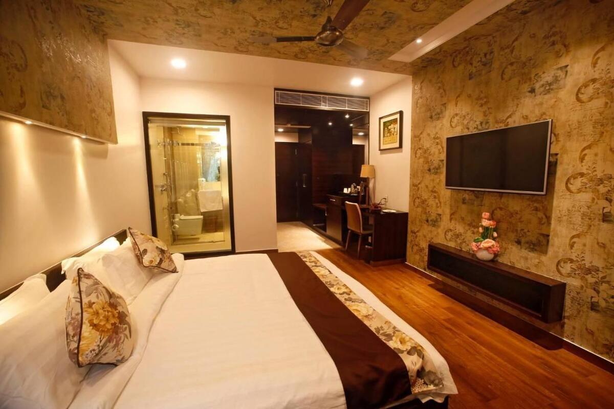 A hotel room with a bed, a desk, a TV, and a shower area.