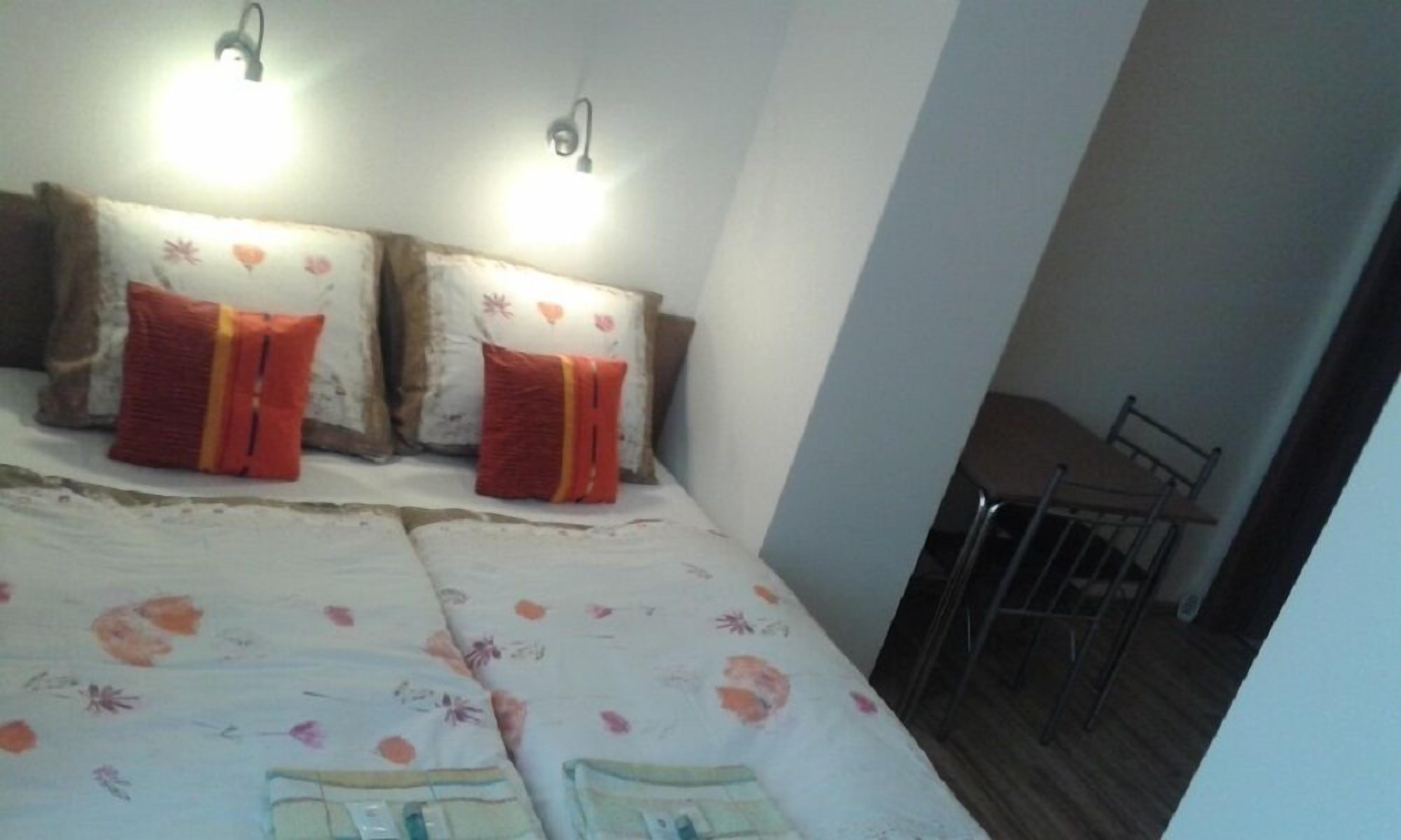 Un dormitorio con una cama, dos luces fijadas a la pared y una mesita cerca de la ventana.